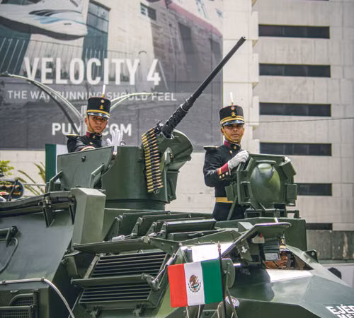Ilustración de militares desfilando con una bandera mexicana frente a edificios; no representa una edición específica.