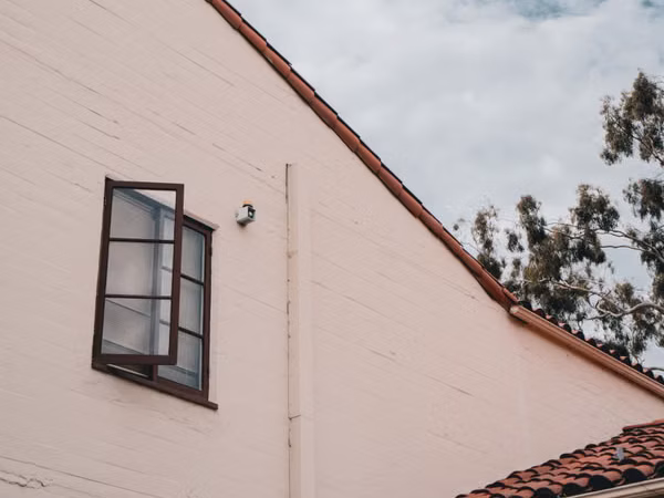 Fachada de vivienda con ventana y alero que proyecta sombra; ilustración editorial sobre ventilación y control solar en el hogar.