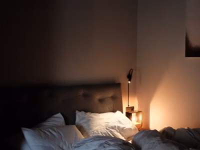 Dormitorio en penumbra con una lámpara encendida y una cama preparada para la noche.