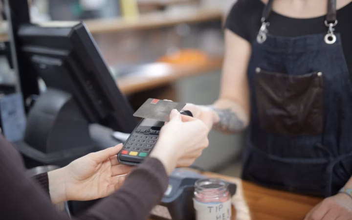 Persona utilizando una terminal para cobrar con tarjeta en un pequeño comercio.